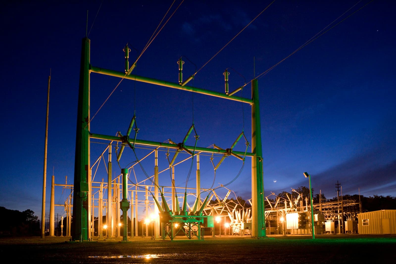 A substation at night with its structures lit against a deep blue sky
