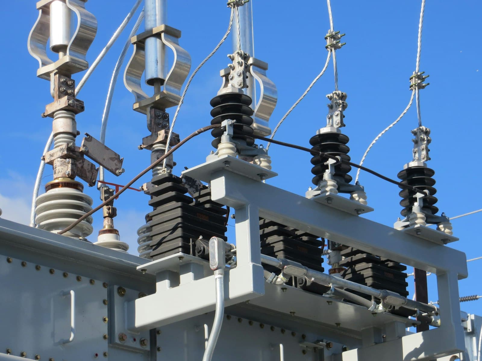 Bushings and surge arresters on top of a substation transformer against a blue sky