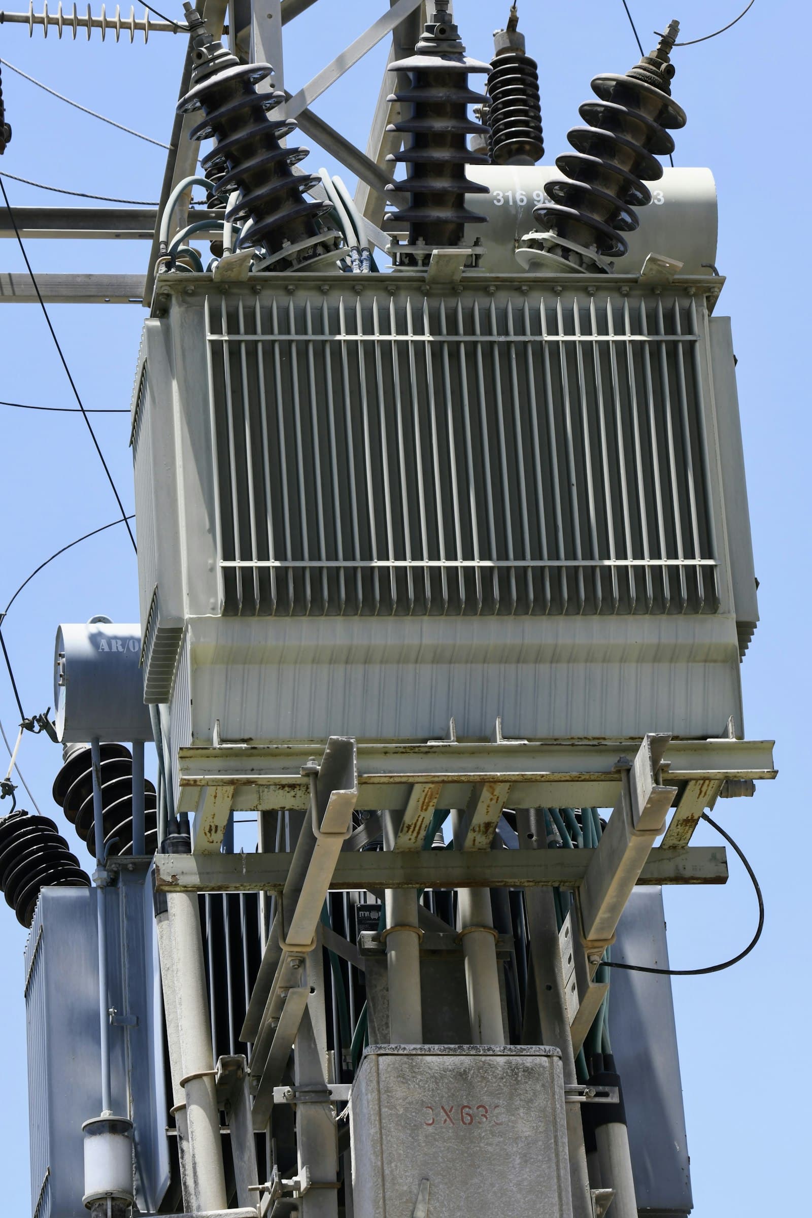 A pole-mounted transformer with radiator fins and bushings against a blue sky